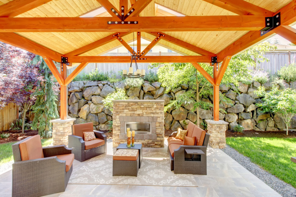 Exterior covered patio with fireplace and furniture. Wood ceiling with skylights.